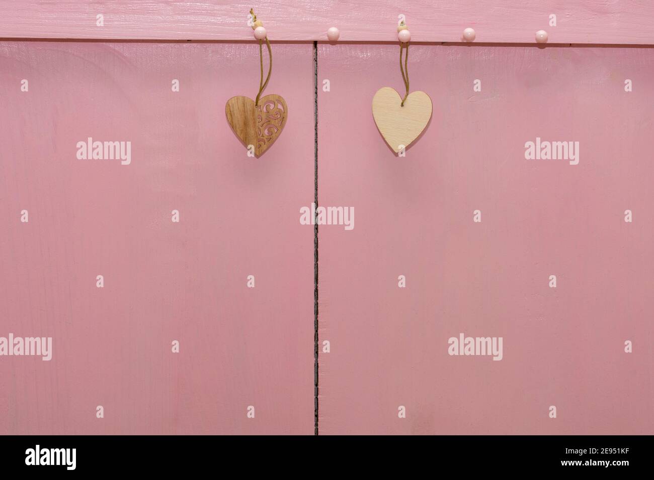 Two small hearts made of wood hang ropes on pink background. Copy space, place for your text. Valentin's day concept, love, wedding. Stock Photo