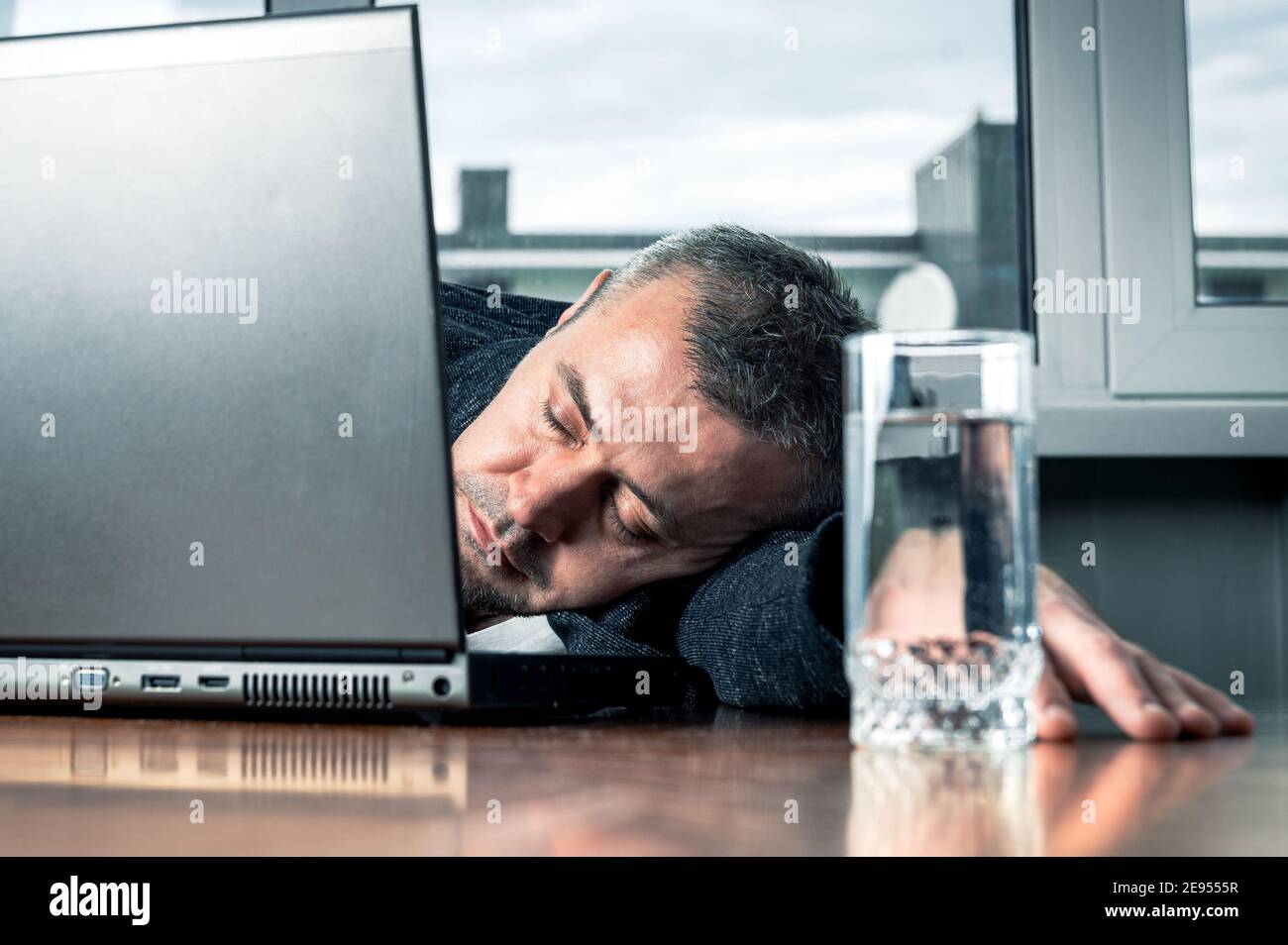 Tired business man sleeps near his laptop. Young bearded tired man sleeping on office table. Work routine concept. Stock Photo