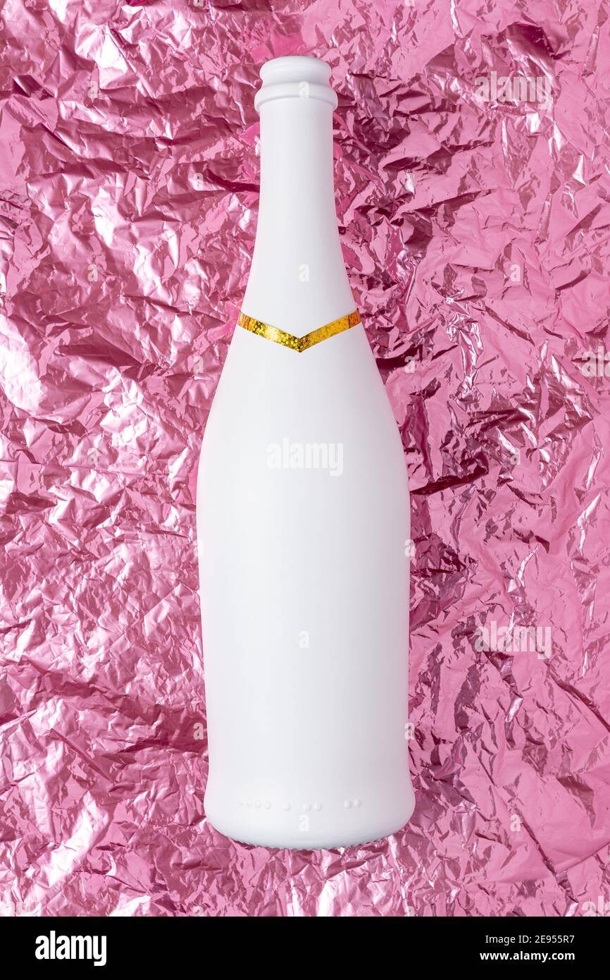 White champagne bottle on pink crumpled foil background. Minimal party
