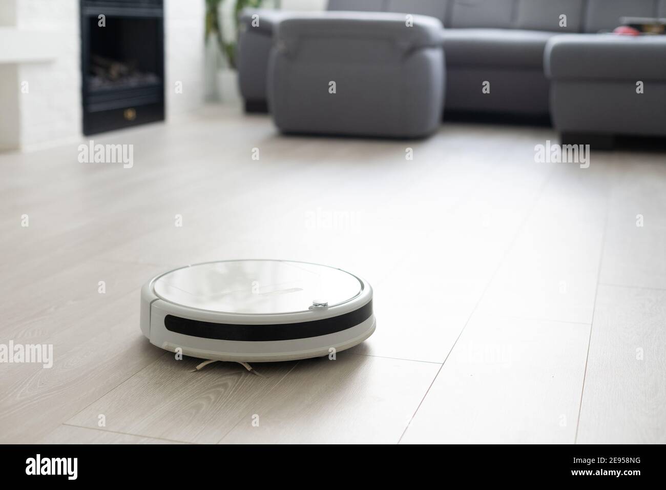White robotic vacuum cleaner on laminate floor cleaning dust in living