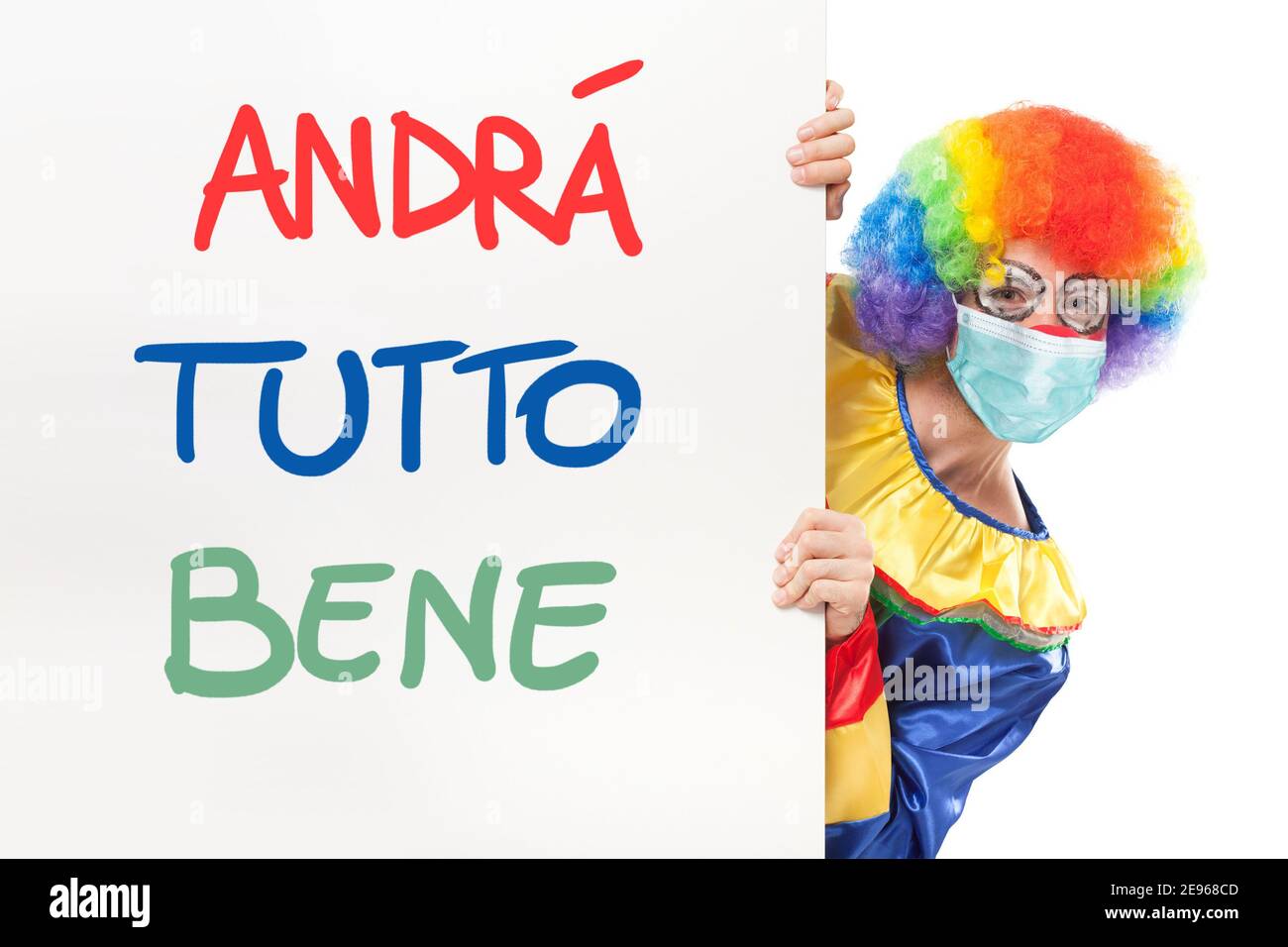 Clown wearing a mask showing a panel with the italian text Andrà tutto bene, which means Everything will be alright. Coronavirus concept Stock Photo