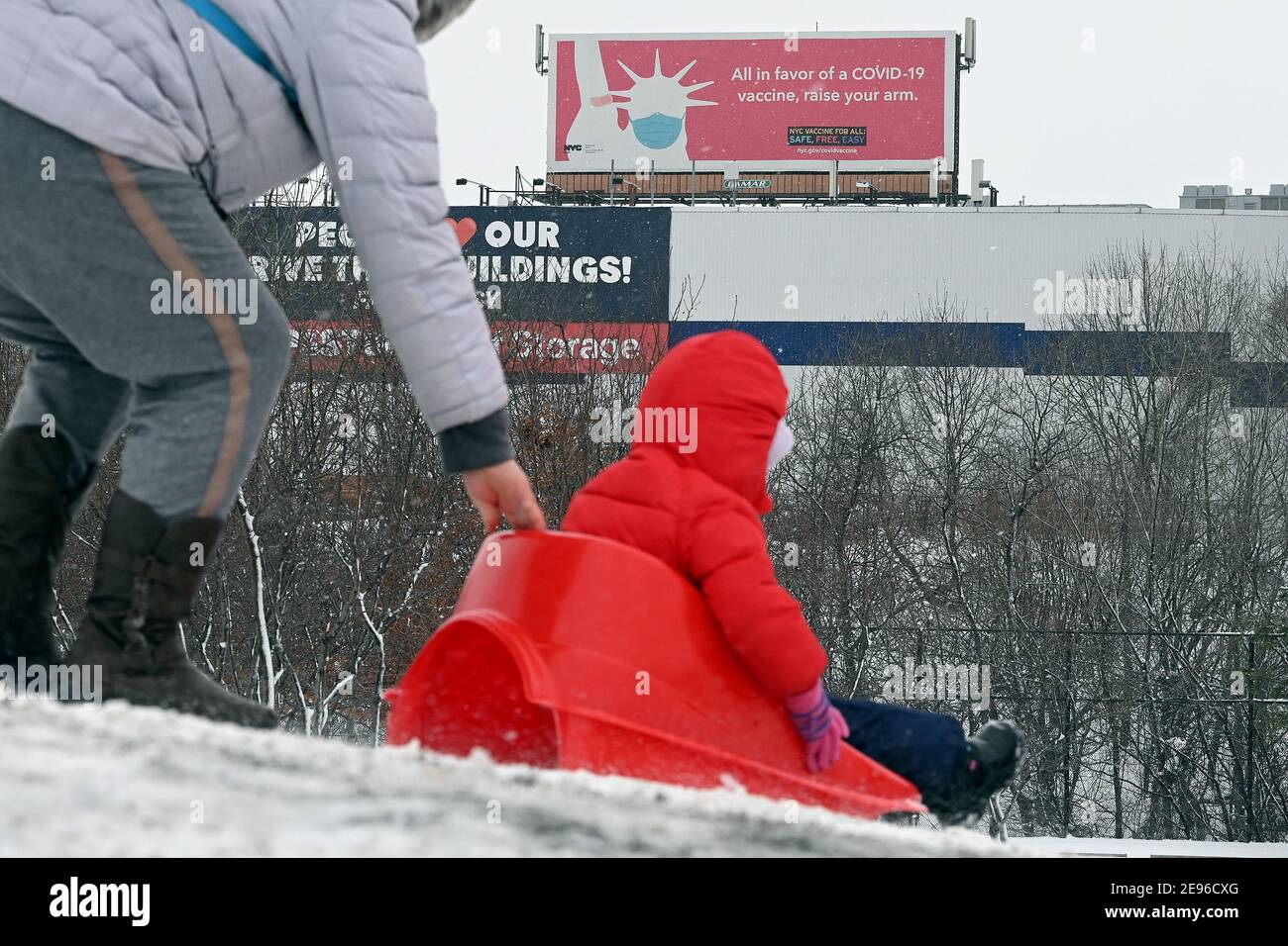 New York, USA. 02nd Feb, 2021. With a COVID-19 Vaccine billboards in the background, a mother pushes her child sitting on a sled atop a snow covered hill in Elmhurst park after a winter storm brought more than 17 inches of snow in parts of the city, in the Queens borough of New York City, NY, February 2, 2021. (Photo by Anthony Behar/Sipa USA) Credit: Sipa USA/Alamy Live News Stock Photo