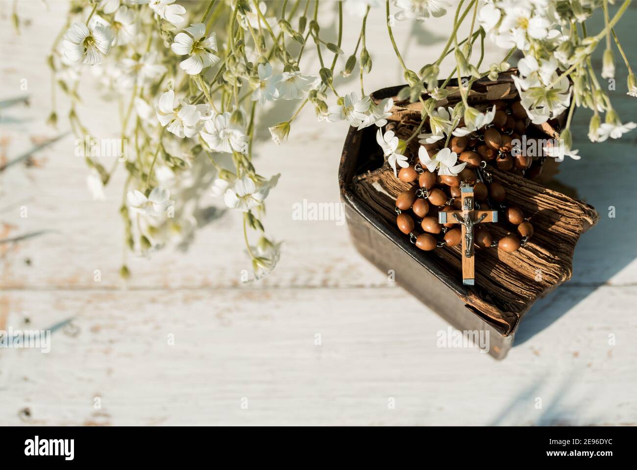 Hands folded in prayer over old Holy Bible. Wooden background.Hands and rosary, prayer, book with yellow pages. white flowers on a background. in the Stock Photo