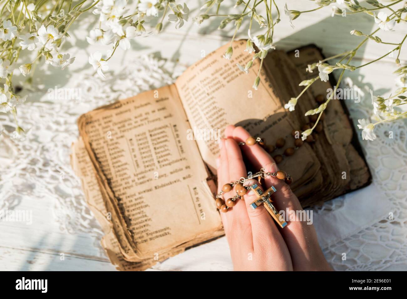 Hands folded in prayer over old Holy Bible. Wooden background.Hands and rosary, prayer, old book with yellow pages. white flowers on a background. in Stock Photo