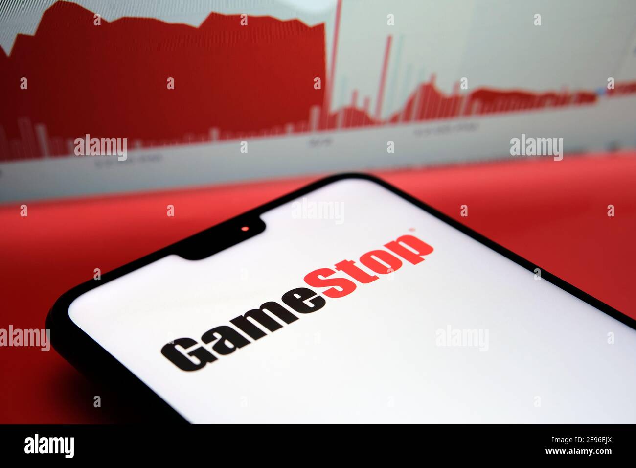 GameStop Corp logo seen on the smartphone and the real chart of GameStop shares (as of 02.02.2021) with the huge plunge seen on the blurred background Stock Photo