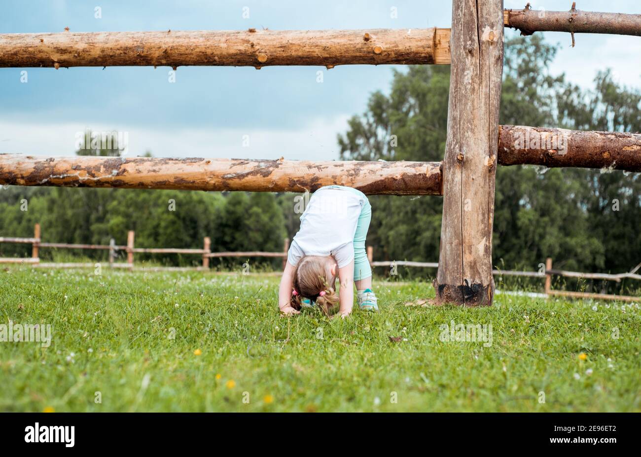 baby girl goes in for sports and yoga outdoors in village by fence, upside down, exercise, healthy lifestyle against the background of the forest Stock Photo