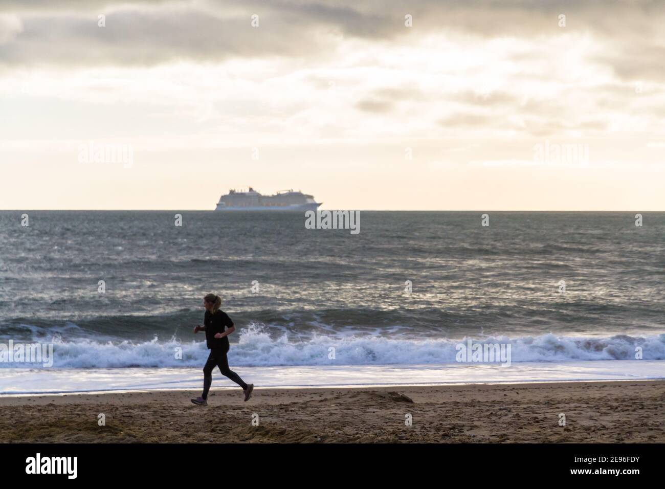 BOURNEMOUTH, ENGLAND - JANUARY 17 2021: Cruise ship moored off Bournemouth at Poole bay, jogger on beach, landscape Stock Photo