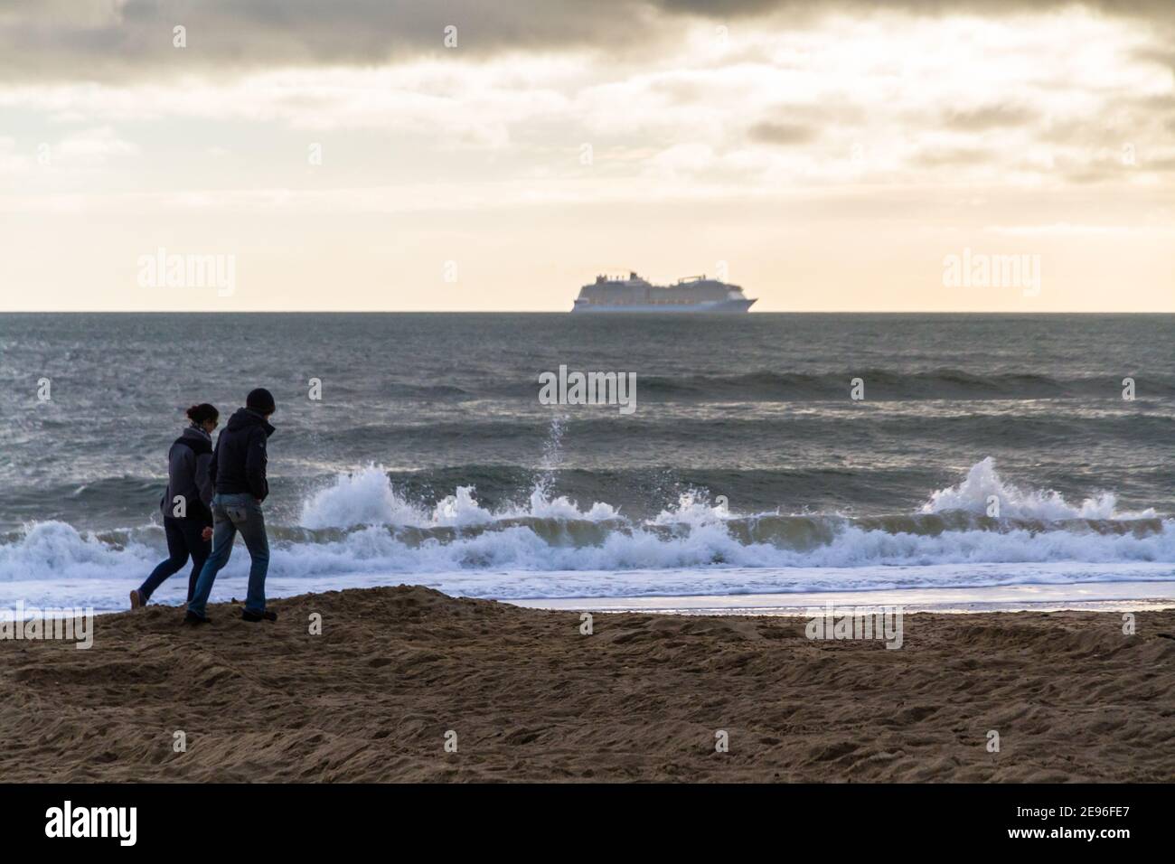 BOURNEMOUTH, ENGLAND - JANUARY 17 2021: Cruise ship moored off Bournemouth at Poole bay, two walkers on beach, landscape Stock Photo