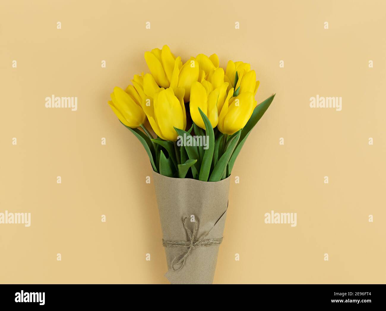Bouquet of yellow tulips wrapped in craft paper on beige background. Stock Photo