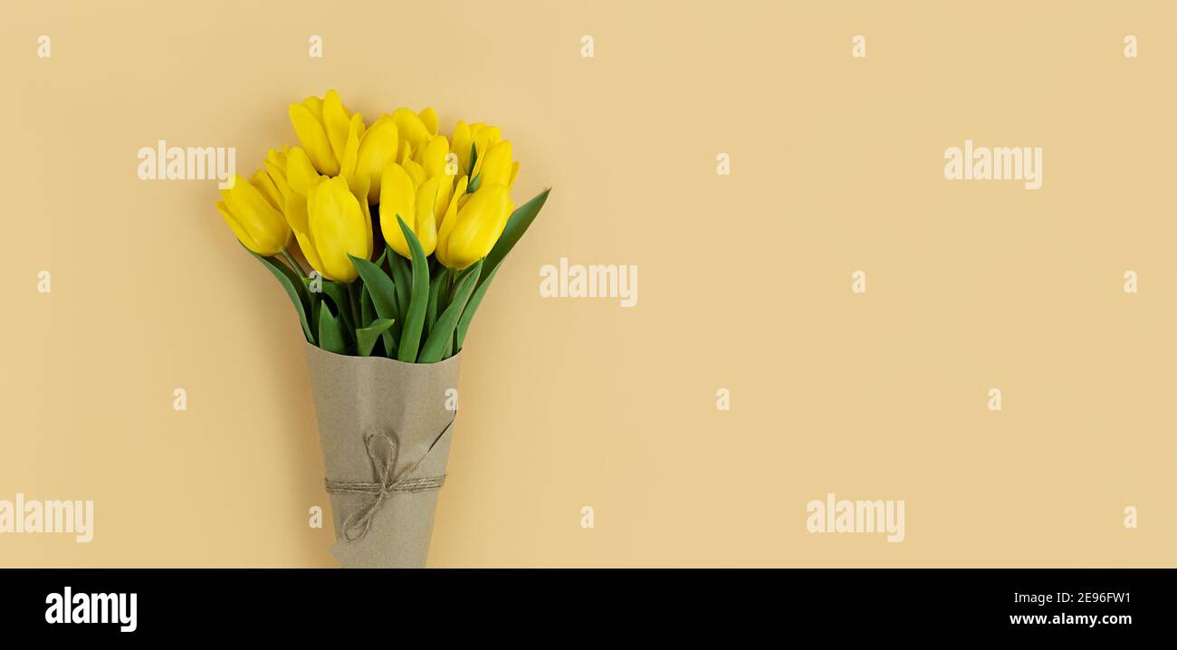 Bouquet of yellow tulips wrapped in craft paper on beige background with copyspace. Stock Photo