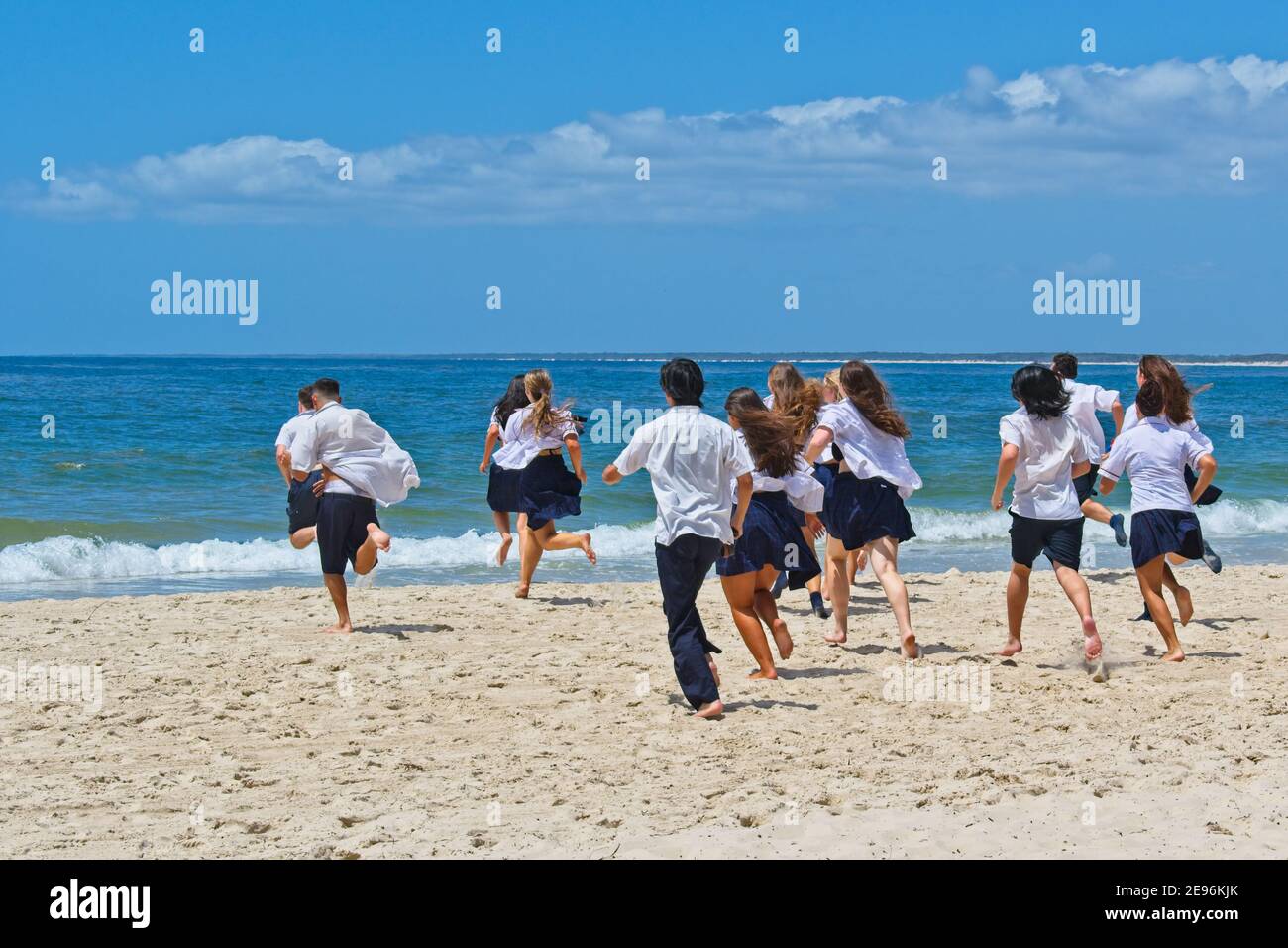 School's out. On their very last day of school - high school students in their school uniforms running traditionally into the ocean Stock Photo