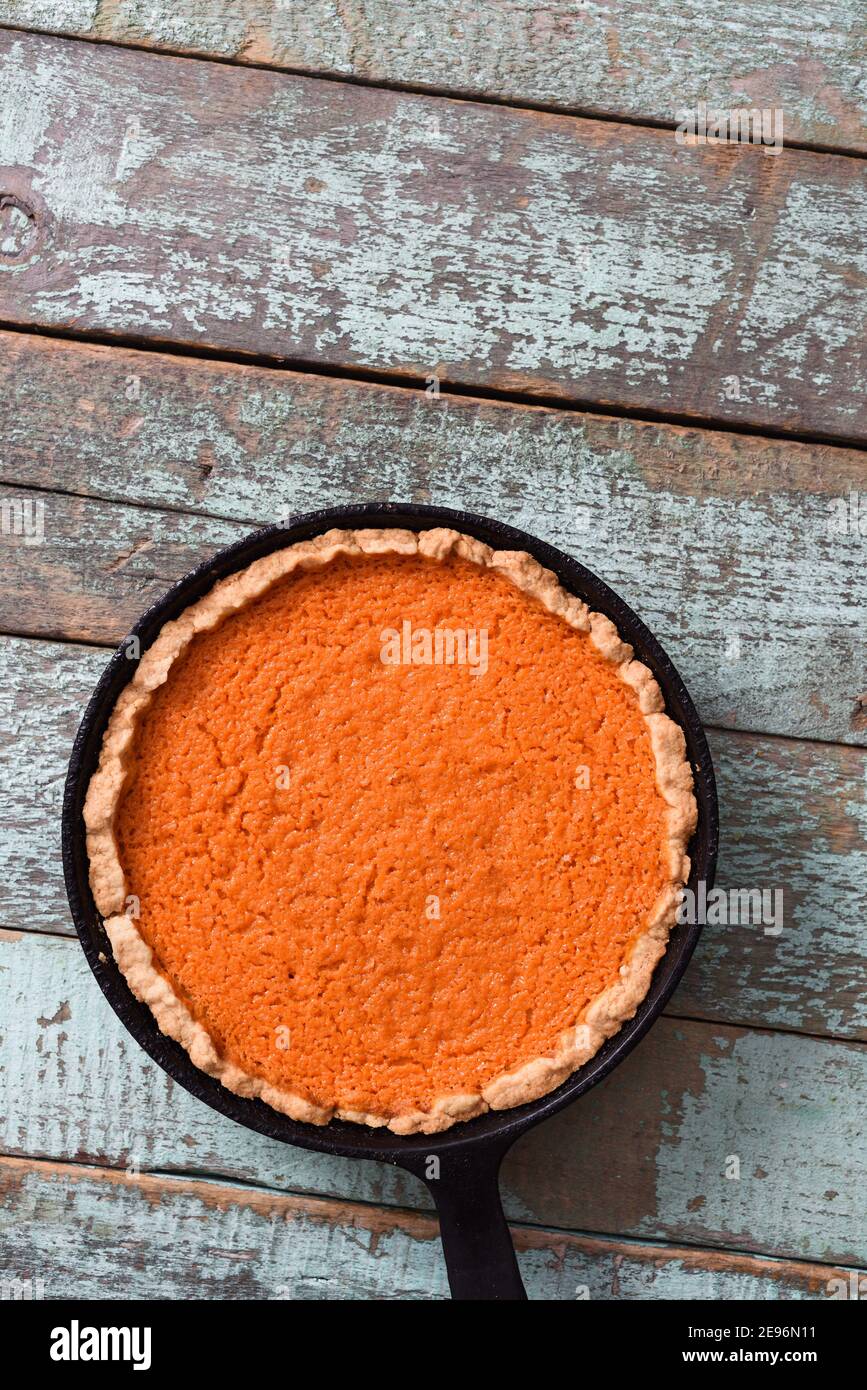 Rustic pumpkin pie in cast iron pan on shabby blue background minimalist style overhead view Stock Photo