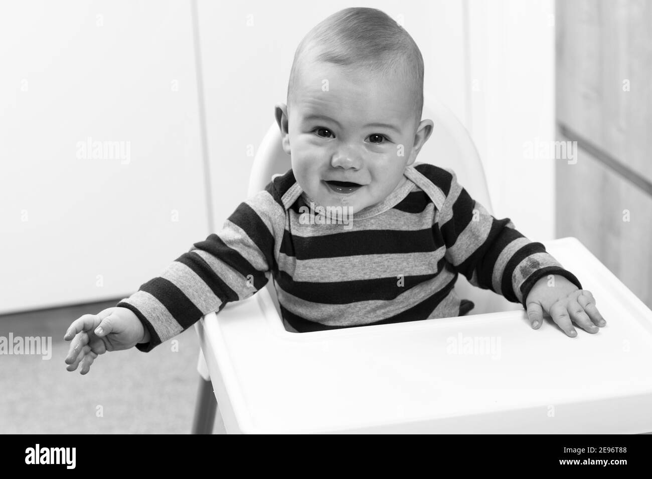 Happy Baby Sitting in High Chair in a White Kitchen Stock Photo