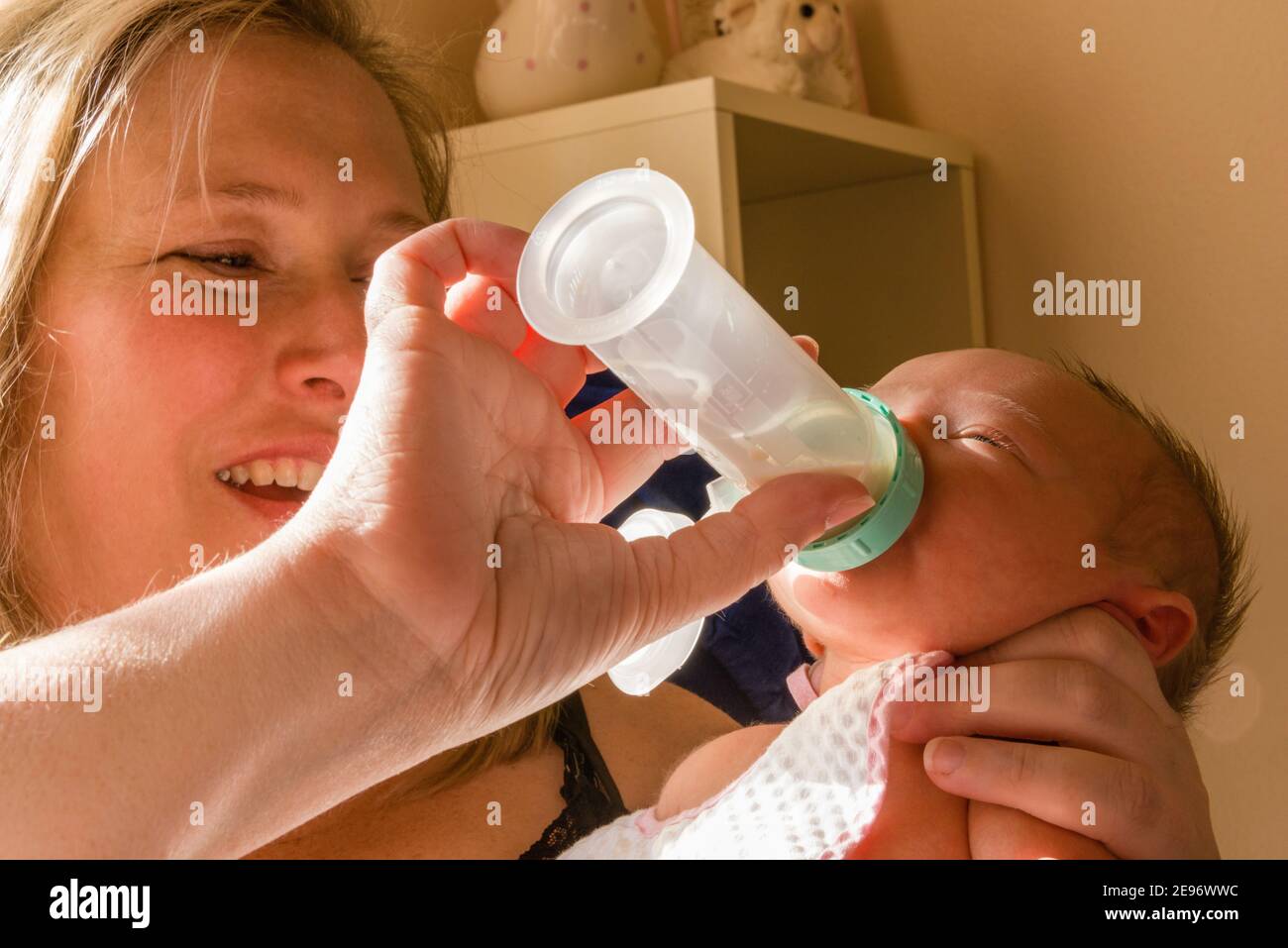 Mother feeding bottle to one-week-old newborn baby girl in baby’s room. Stock Photo