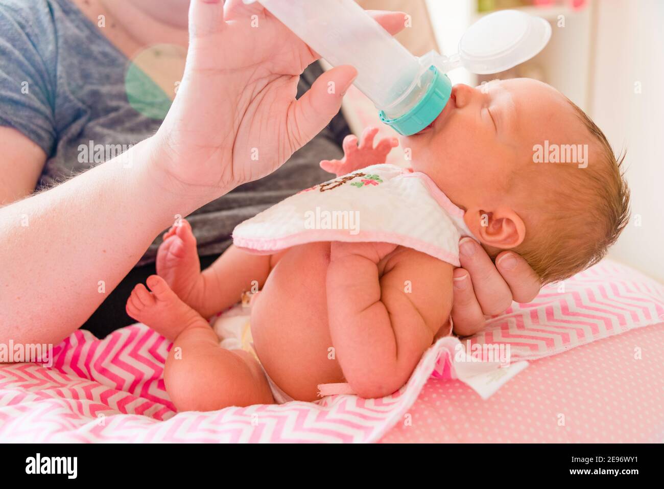 Mother holding and feeding bottle to newborn baby girl in baby’s room. Stock Photo