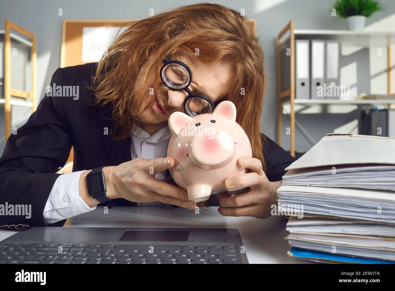Funny man sitting in office and looking inside piggy bank to see if ...