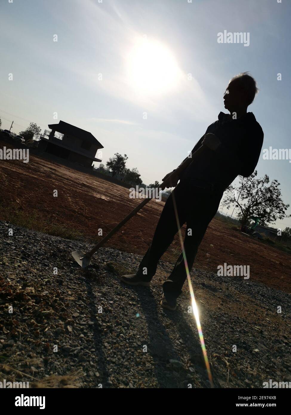 Silhouette of an old man holding a hoe on the vacant land before cultivation. Stock Photo