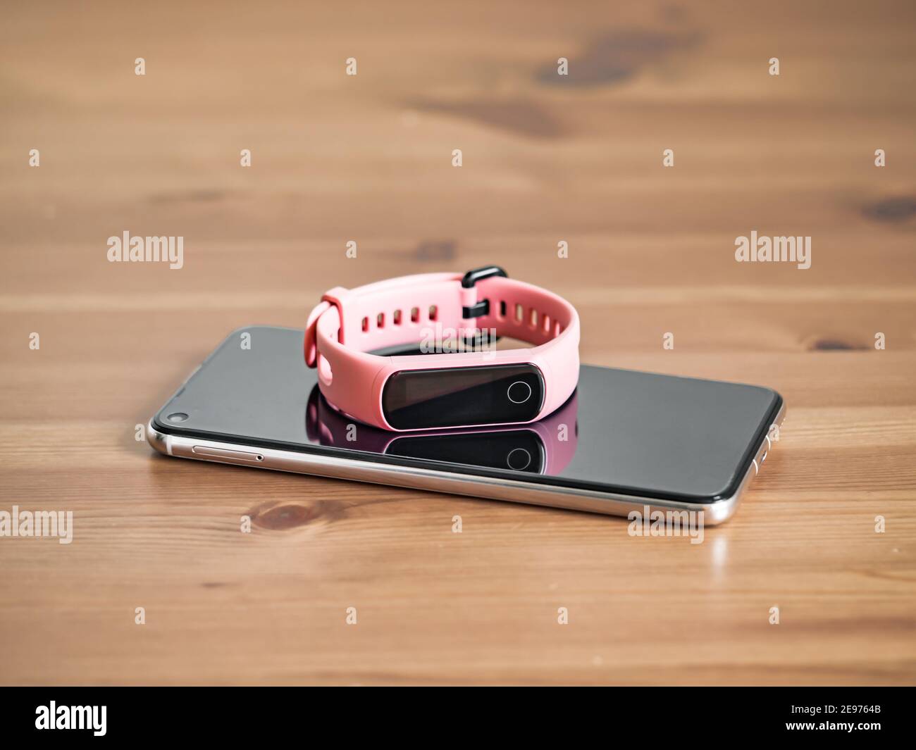 Fitness tracker on smartphone wooden tabletop. Pink female pedometer or wearable device on