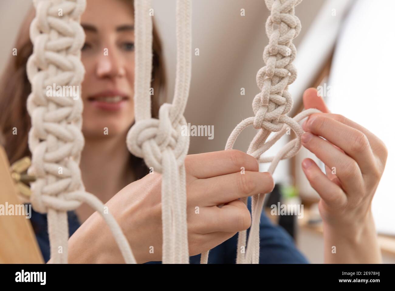 Woman relaxing and making macrame at home with different knots on a sunny day at home in attic. Stay at home hobbies. Stock Photo