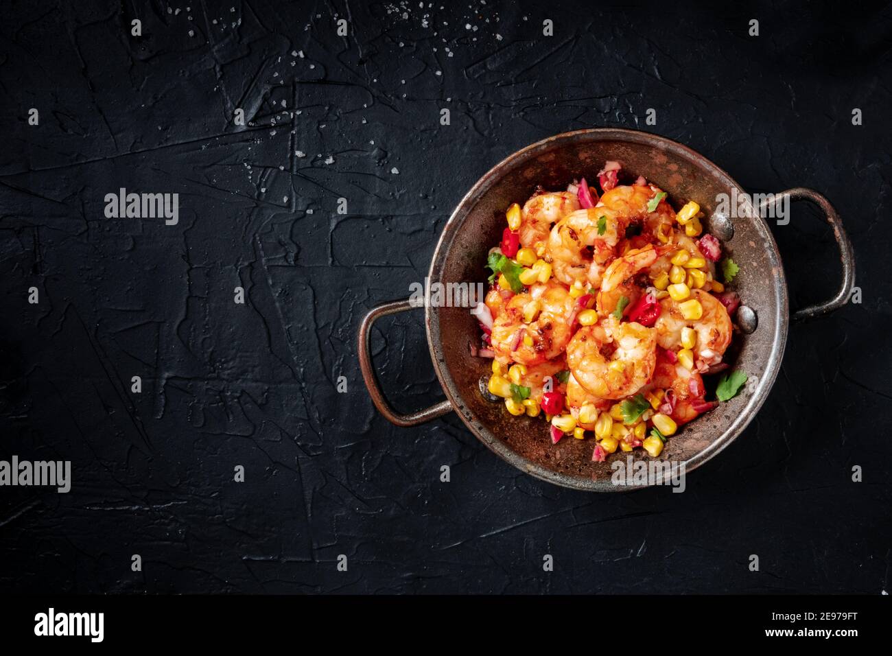 Spicy shrimps with vegetables in a skillet, overhead shot on a black background with a place for text Stock Photo