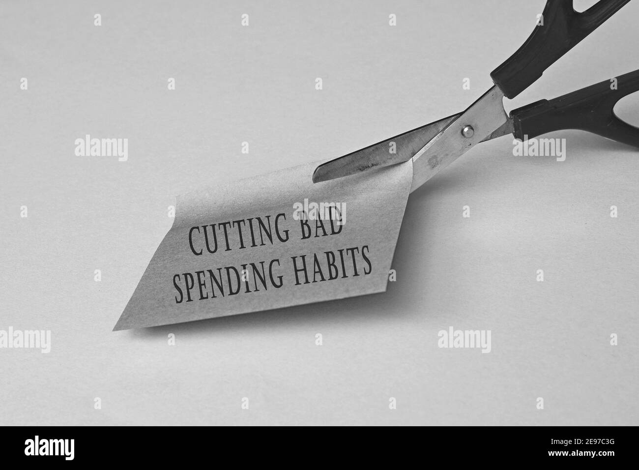 Scissors that cut yellow notepad with text on a black and white background. Spending habits concept Stock Photo