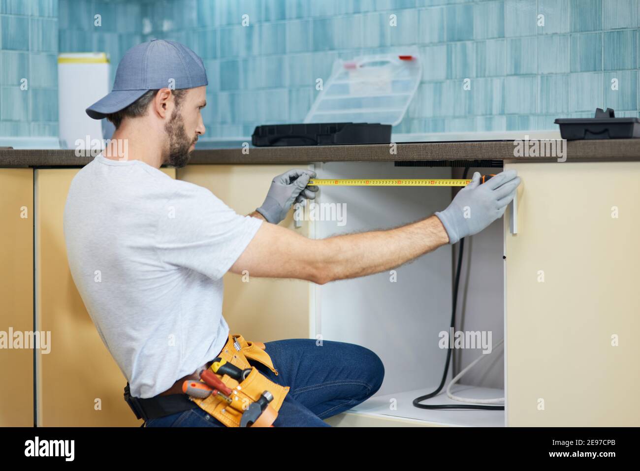 Young repairman, professional plumber using measure tape while doing plumbing work in a new flat