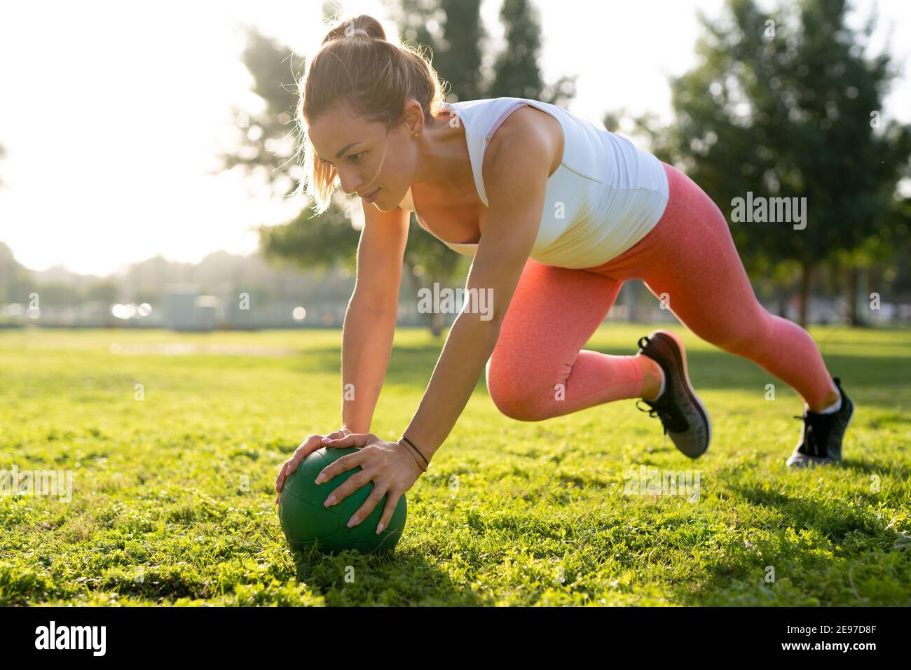 A youthful woman engages in exercises amidst the greenery of the park ...