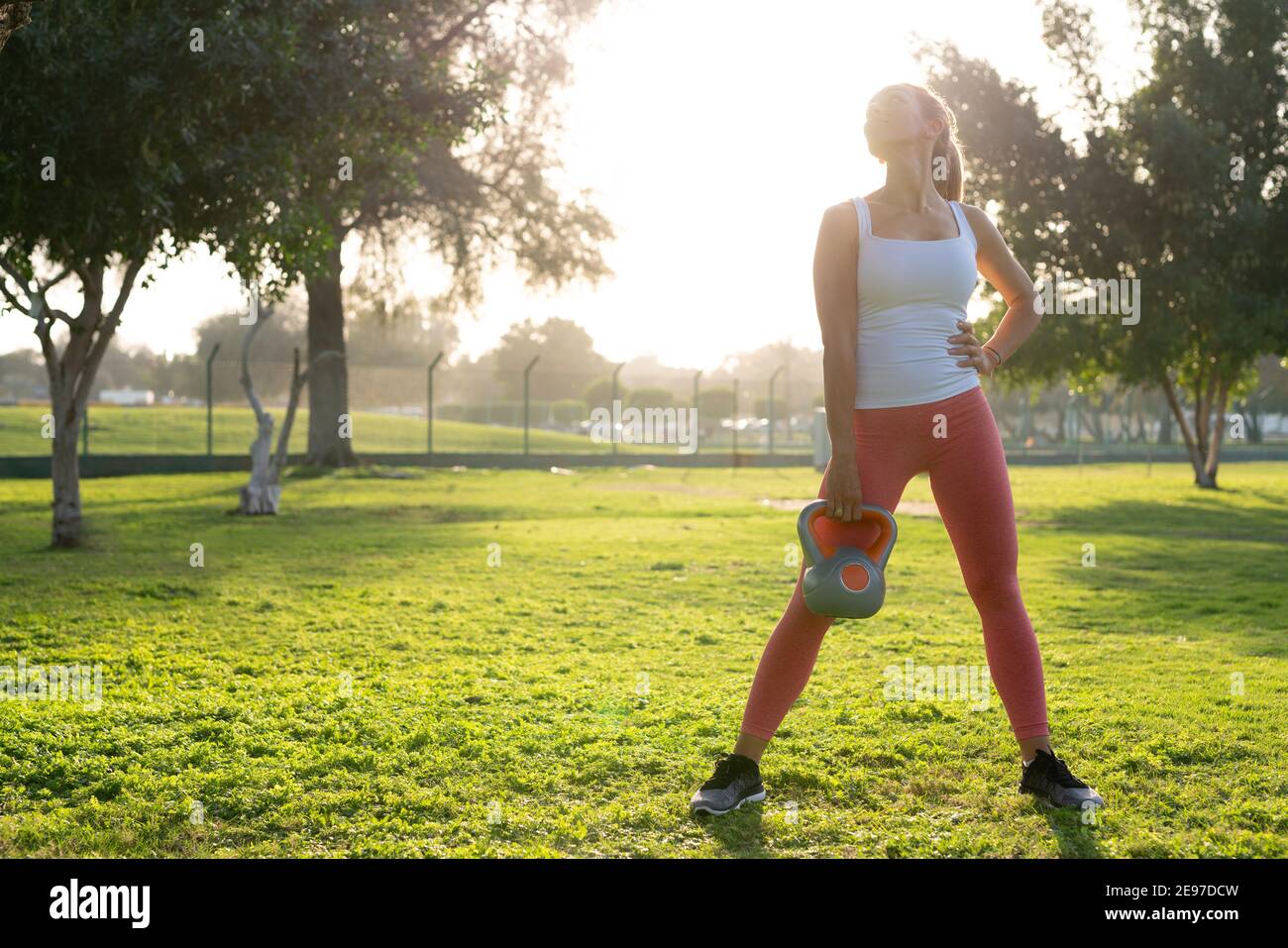 A youthful woman engages in exercises amidst the greenery of the park ...