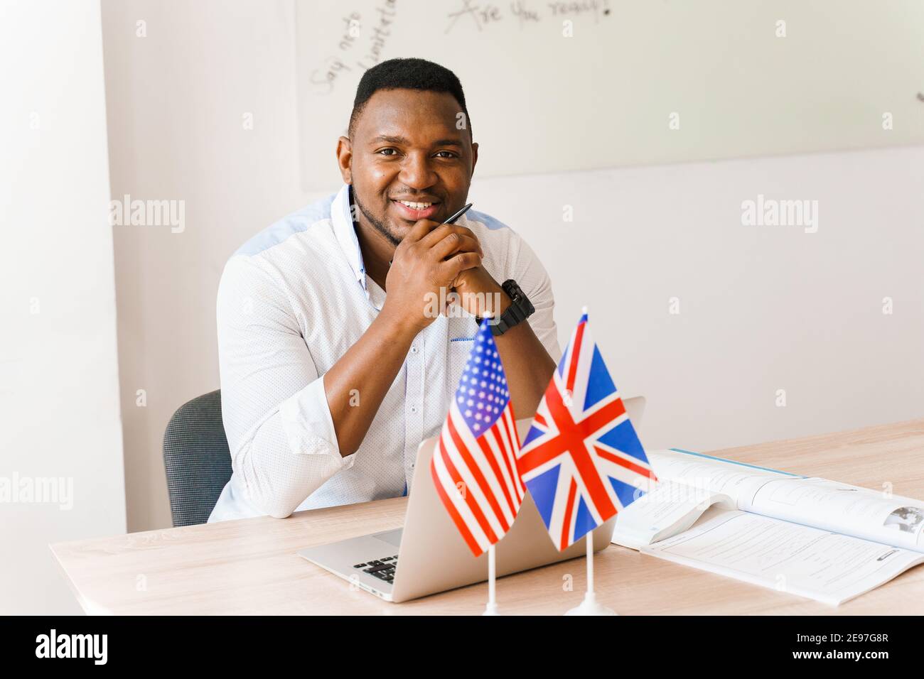 English and British flags in front. Black handsome translator uses his laptop for online work according social distancing. Scientist works at home on Stock Photo
