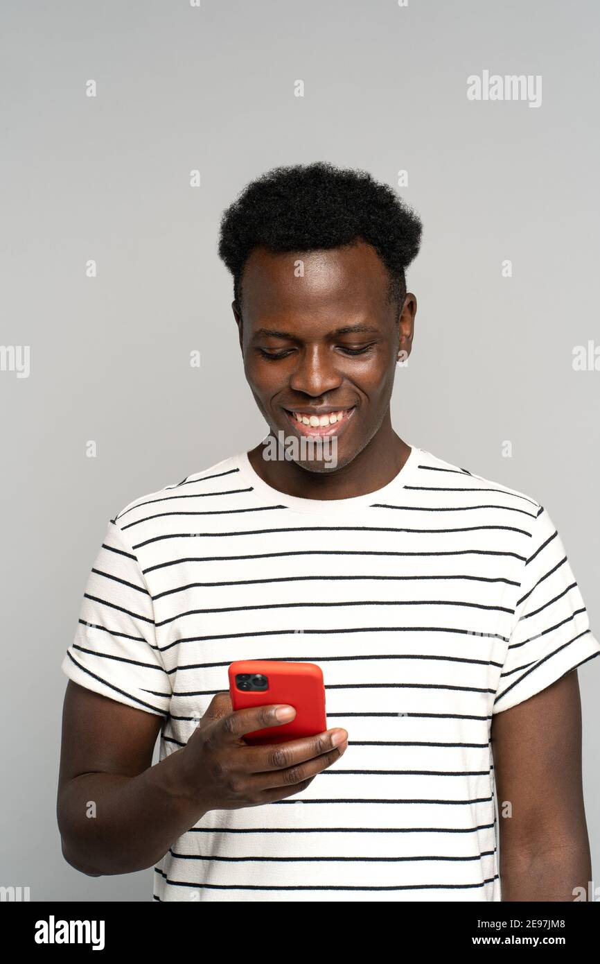 Happy African millennial man in glasses, holding mobile phone, isolated on studio grey background Stock Photo
