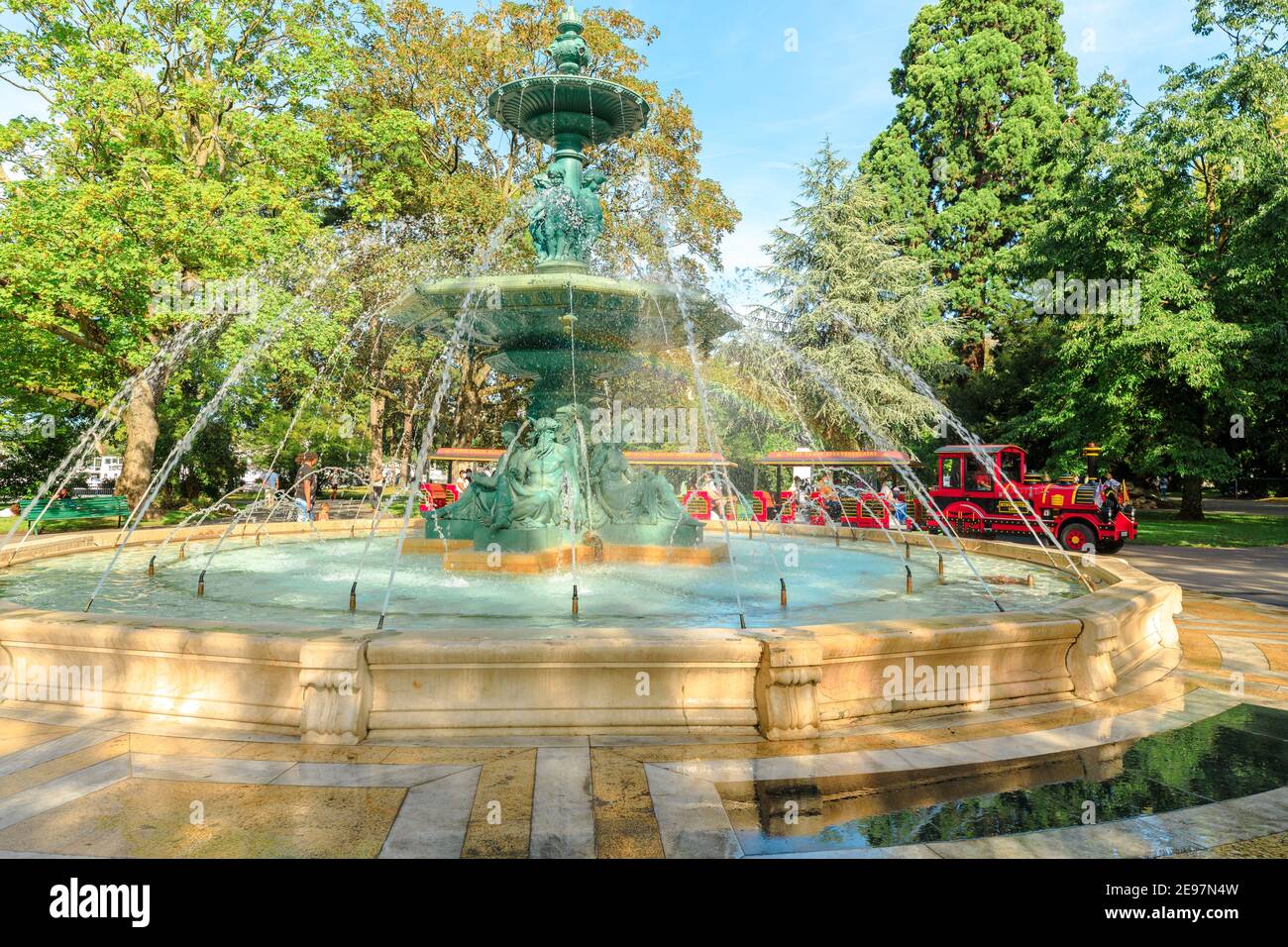 Geneva, Switzerland - Aug 15, 2020: Fountain of Four Seasons in center of Jardin Anglais with Red tourist train with carriages and locomotive along Stock Photo