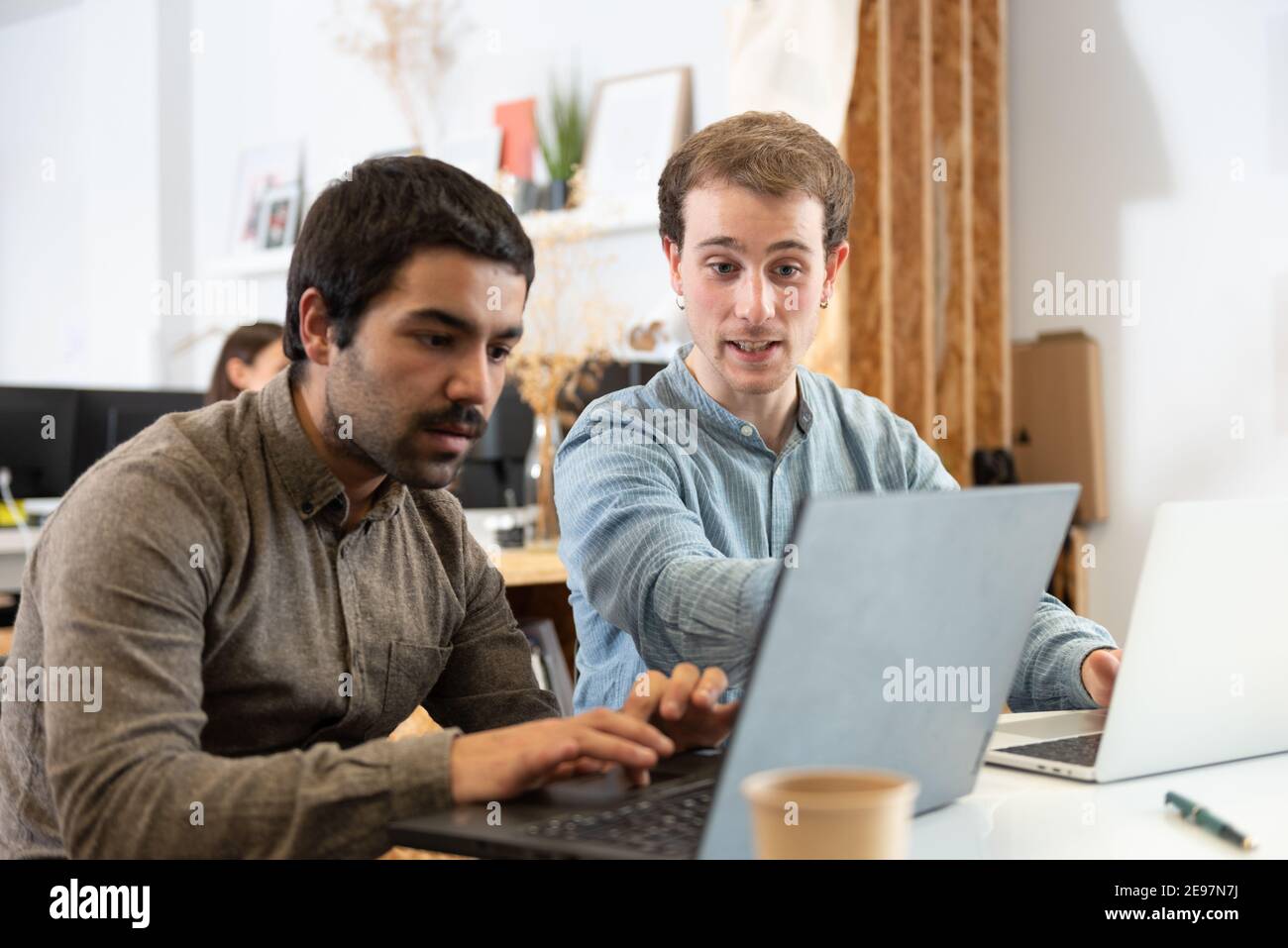 Coworkers helping each other while working on their laptops in the office. Stock Photo