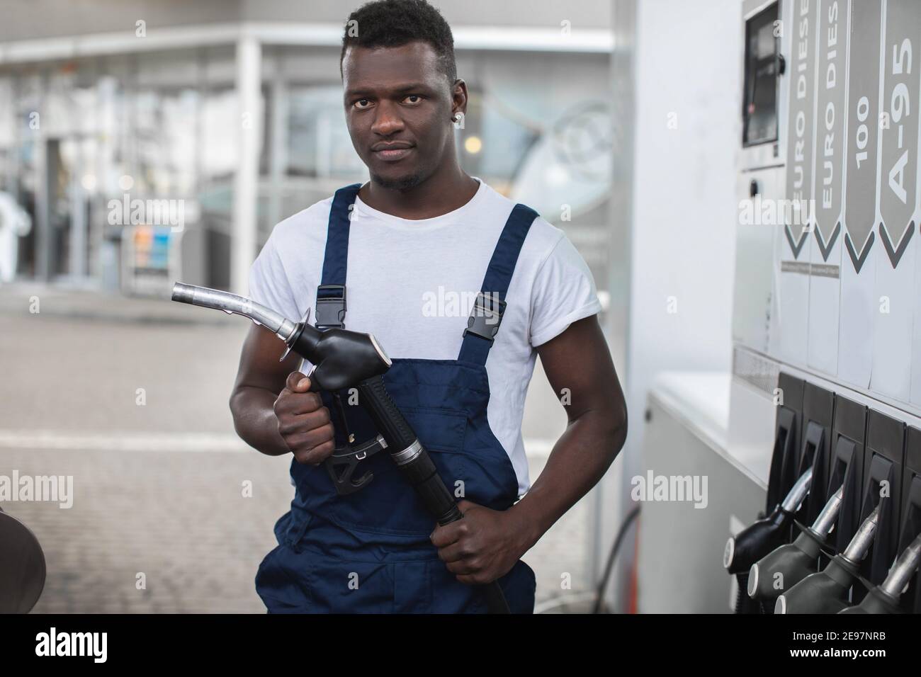 Handsome young African guy, gas station worker, wearing white tshirt and blue overalls and
