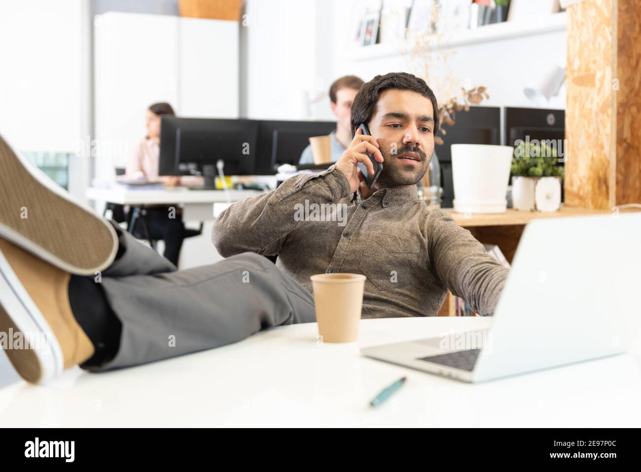 A relaxed hispanic man with mustache whith his feet on desk talking on the phone in the office. Stock Photo