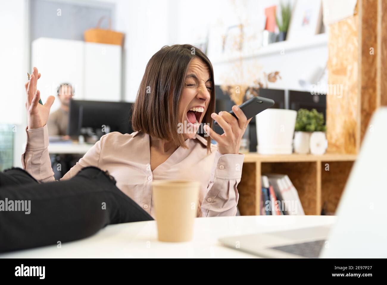 An angry hispanic woman whith her feet on desk yelling on the phone in the office. Stock Photo