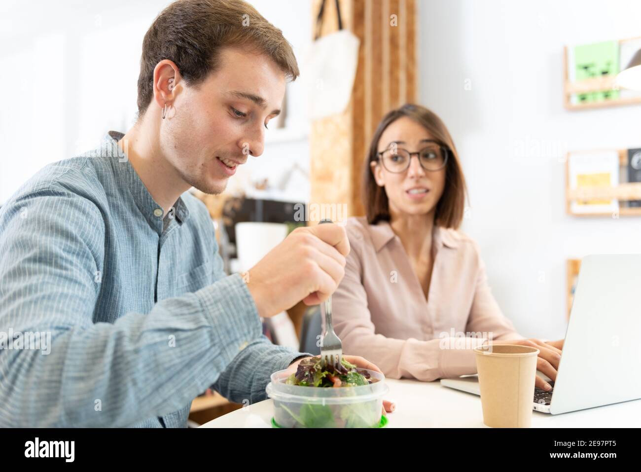 A handsome man chatting with a coworker while eating a salad. Healthy nutrition habits in the office concept. Stock Photo