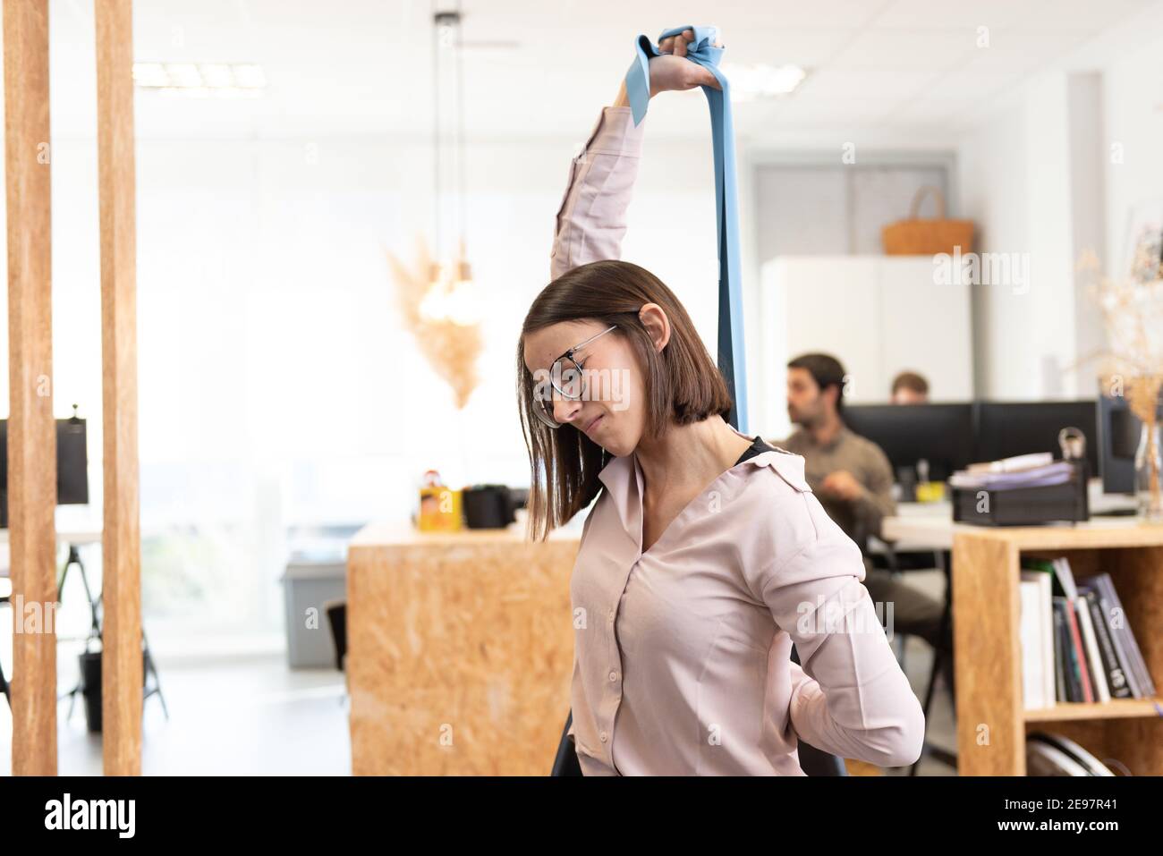 Healthy lifestyle in the workplace concept. Woman with backache or back pain  stretching with a pilates rubber band in the office. Stock Photo