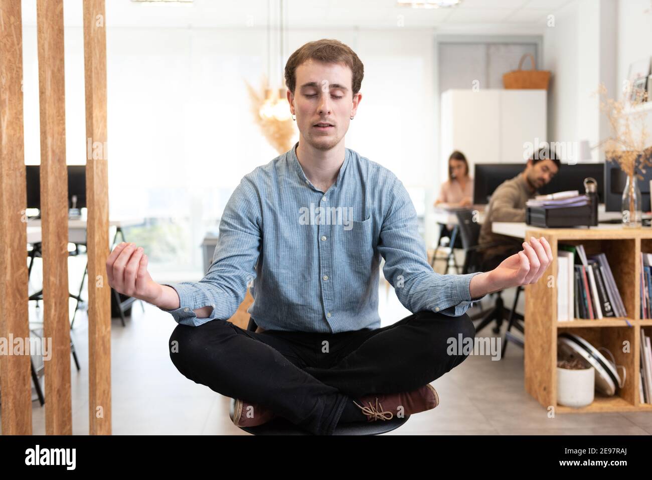Handsome man meditating while sitting crossed legs on a chair in the office. Stock Photo