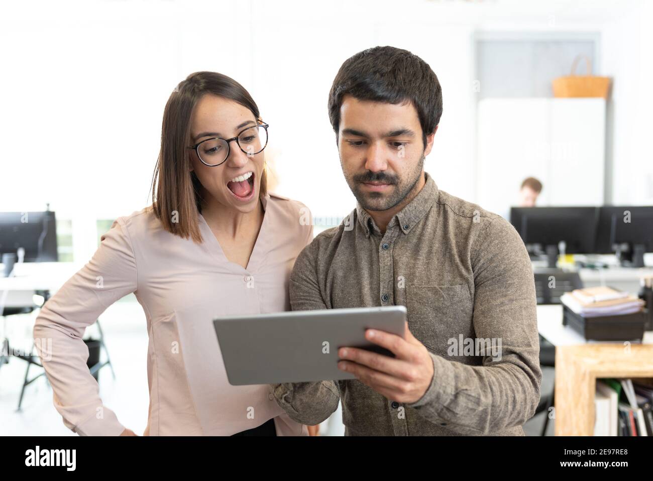 Hispanic proud man showing something to a surprised coworker on his tablet at the office. Stock Photo
