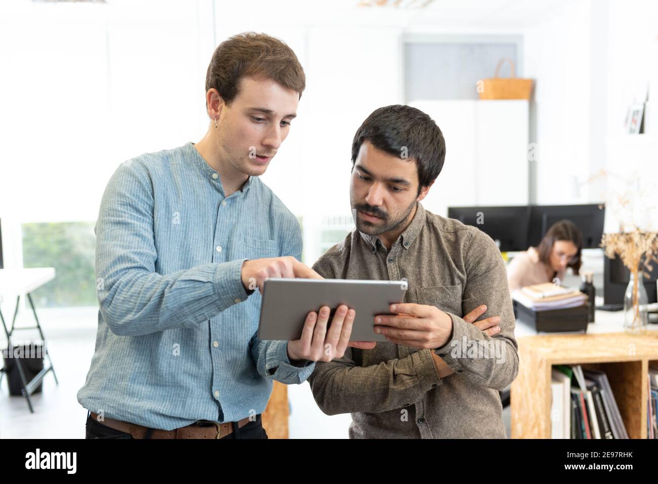 Diverse male coworkers chating and giving their opinion while looking a tablet at the office. Stock Photo