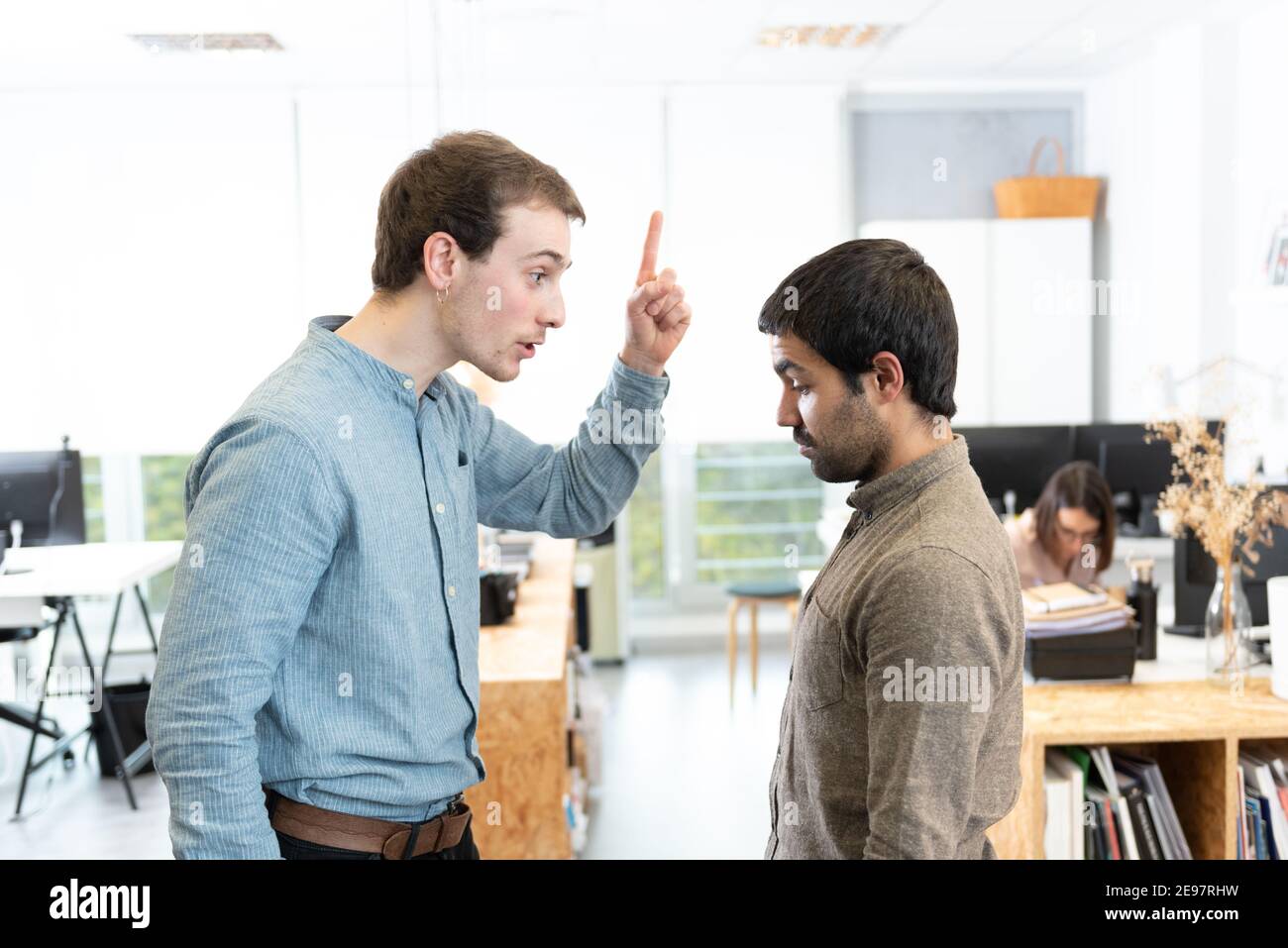 Handsome young man threatening his  sad hispanic coworker at the office. Stock Photo
