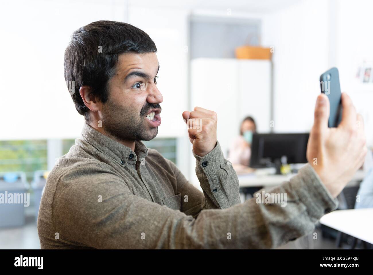 Angry hispanic man with mustache threatening with his fist up while looking at the phone Stock Photo