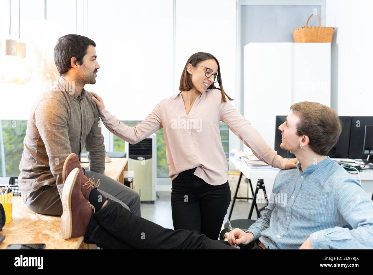 Three diverse young coworkers chatting relaxed at the office. Stock Photo