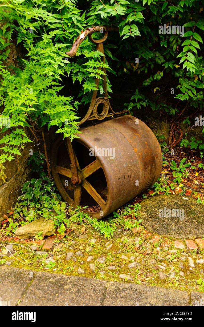 An old fashioned cast iron lawn or grass roller left in an overgrown corner ideal for horticulture or gardening concepts Stock Photo