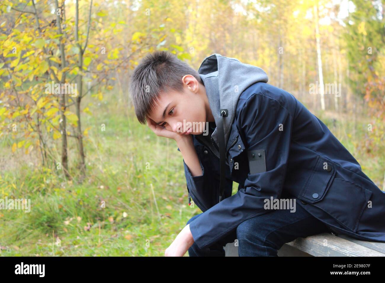 Sad teenage boy sitting on a bench in an autumn park Stock Photo