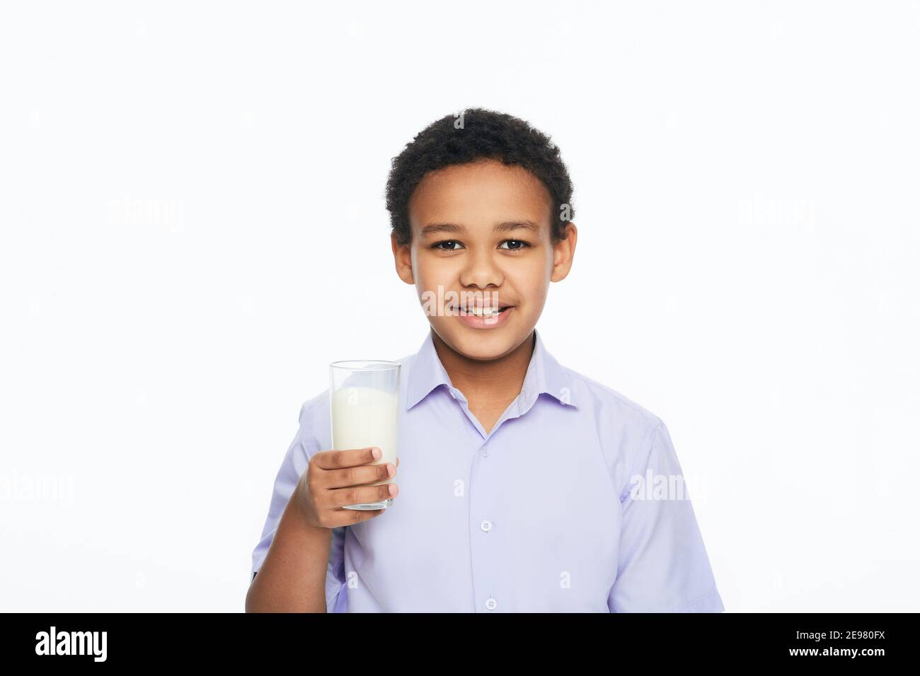 African American male kid holding a glass of milk with a toothy smile, isolated on white background. Benefits of milk for kids Stock Photo