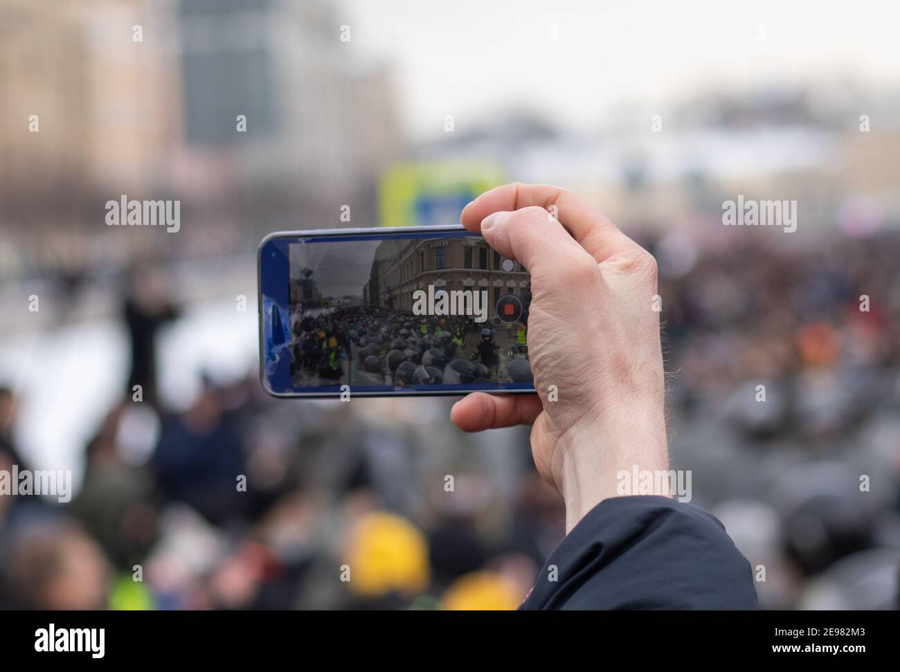 Hand with phone filming video. Police and protest demonstration on screen. Display with crowd of people, blurry background with copy space Stock Photo