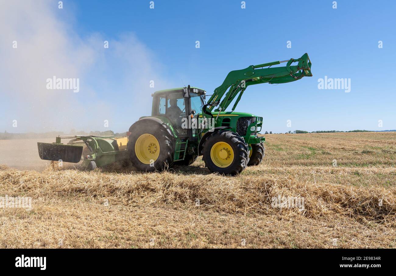 Tractor with straw rake and dust cloud on a stubble field Stock Photo