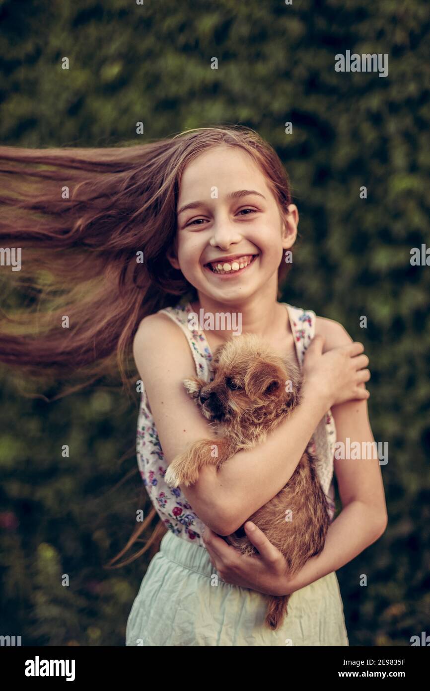 A little blond girl with her pet dog outdooors in park. The girl loves ...