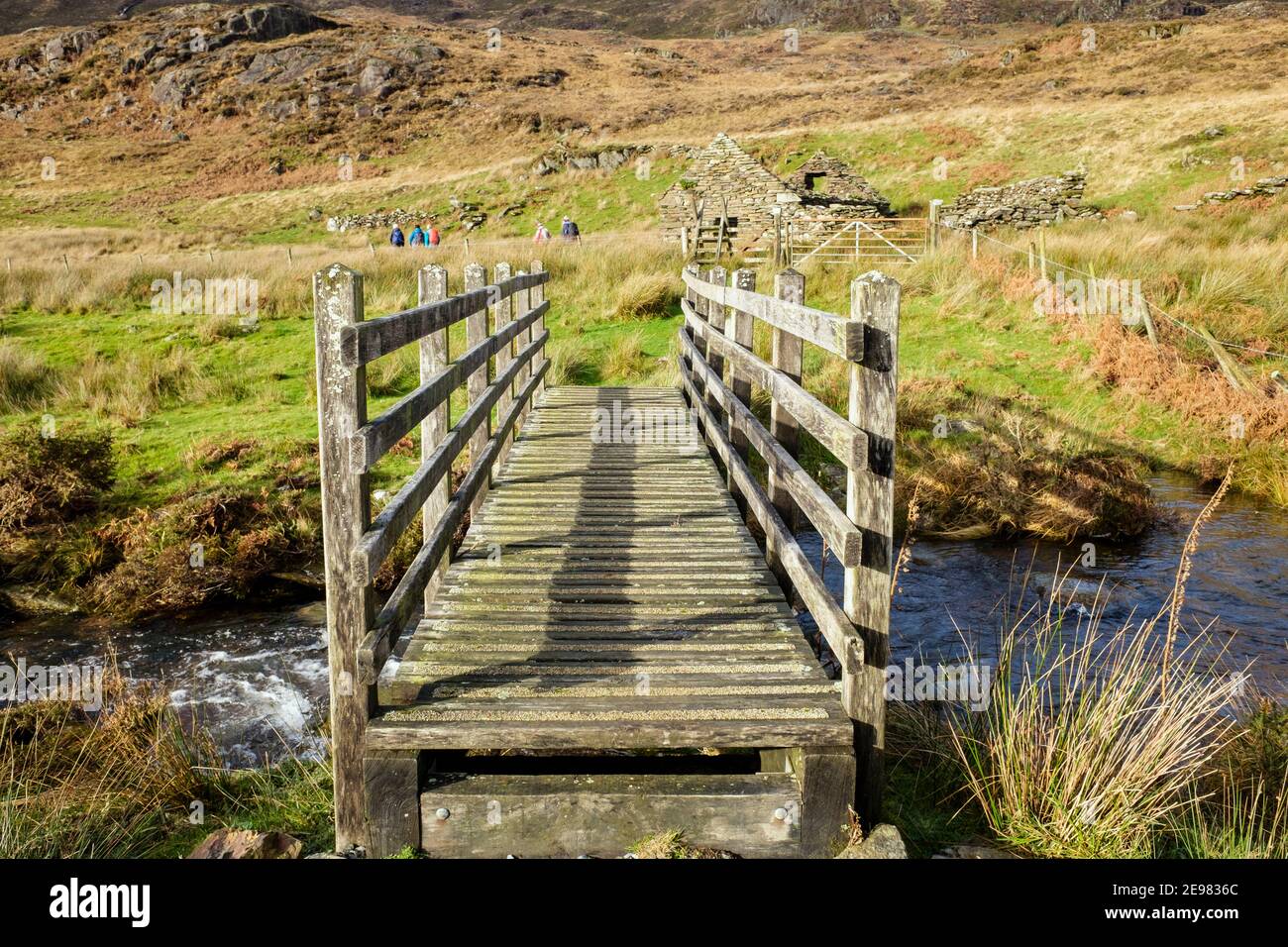 Wooden footbridge crossing a stream with distant walkers on footpath in Snowdonia National Park. Bethania, Beddgelert, Gwynedd, Wales, UK, Britain Stock Photo